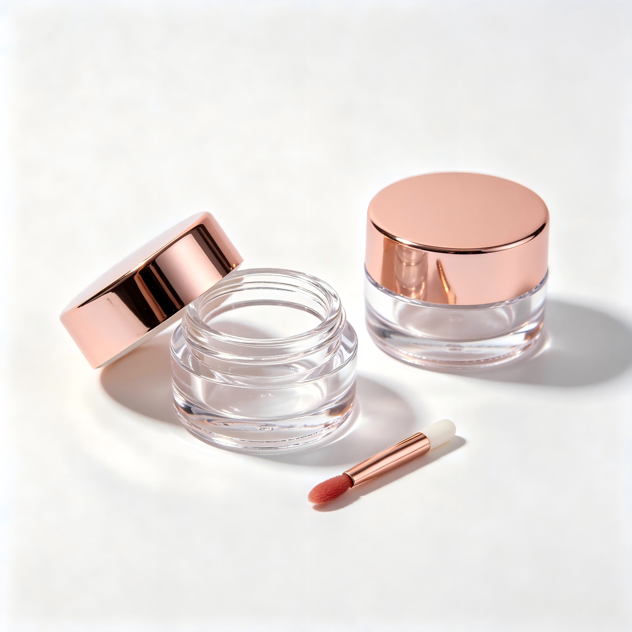Clear small lip gloss jar with shiny rose gold metal lid and matching lip applicator wand for cream lip glaze